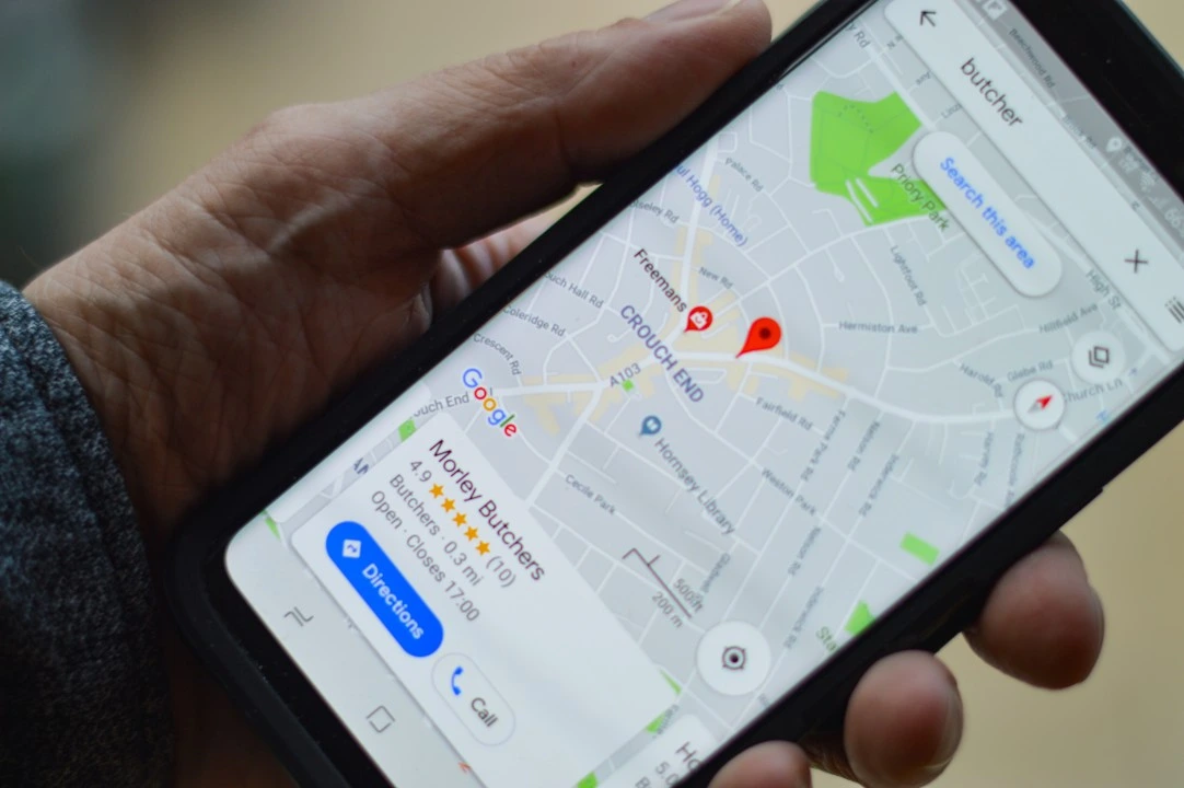 A close-up of a person holding a smartphone displaying a Google Maps search for a local butcher in the Crouch End area, showing business details and a 4.9-star rating.